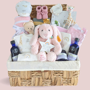 Baby girl gifts for a newborn in a hamper basket with pink presents.