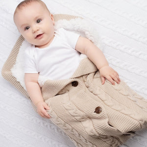 Biscuit coloured cable knit baby sleeping pouch / swaddle. The ideal cosy wrap to keep baby snug and warm.