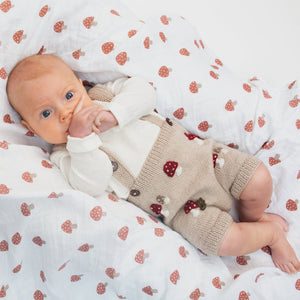 A baby lying on a swaddle blanket with a mushroom print.