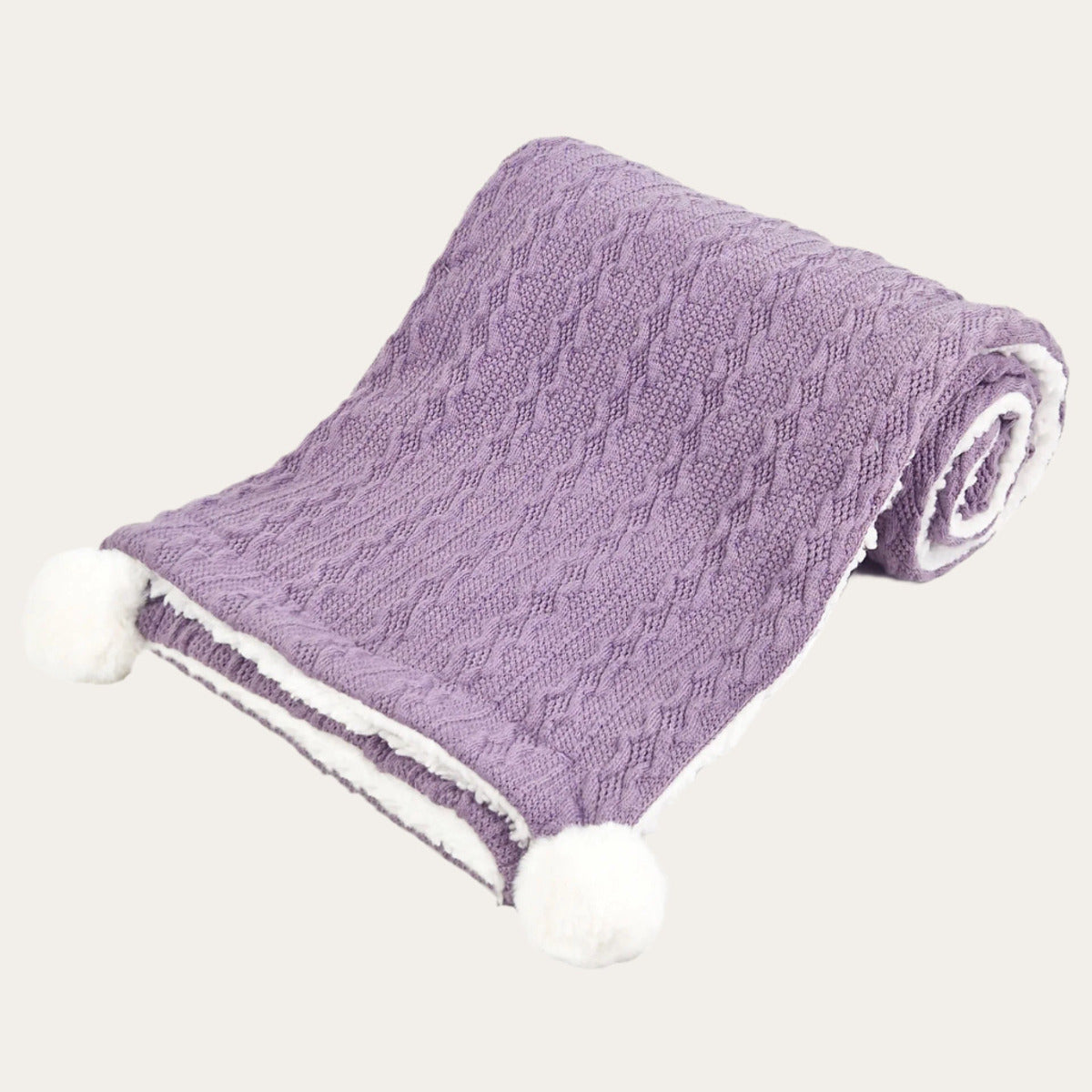 Purple cable knit baby blanket with pom poms a the corners in a light purple lilac colour
