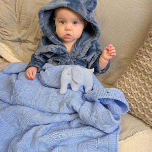 Mid sky blue recycled cable knit baby blanket with pom poms, shown with a baby sitting up.