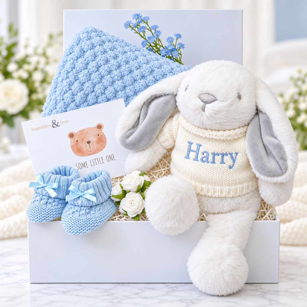 Baby boy gifts hamper with white bunny soft toy and blanket. Presents are packed in a gift box.