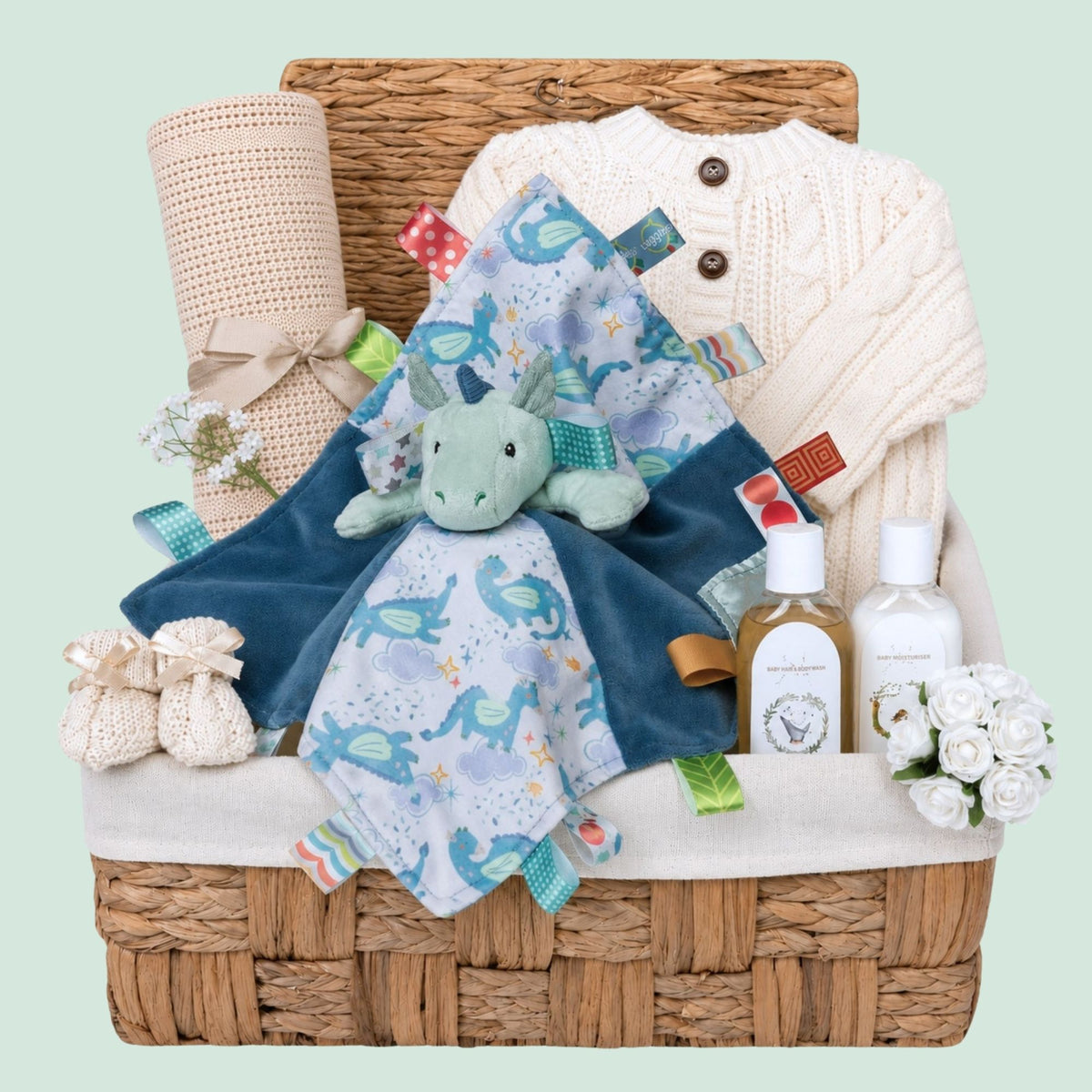 New baby boy gifts in a hamper basket, presents include dragon taggie comforter, baby essentials and cream knitted cardigan
