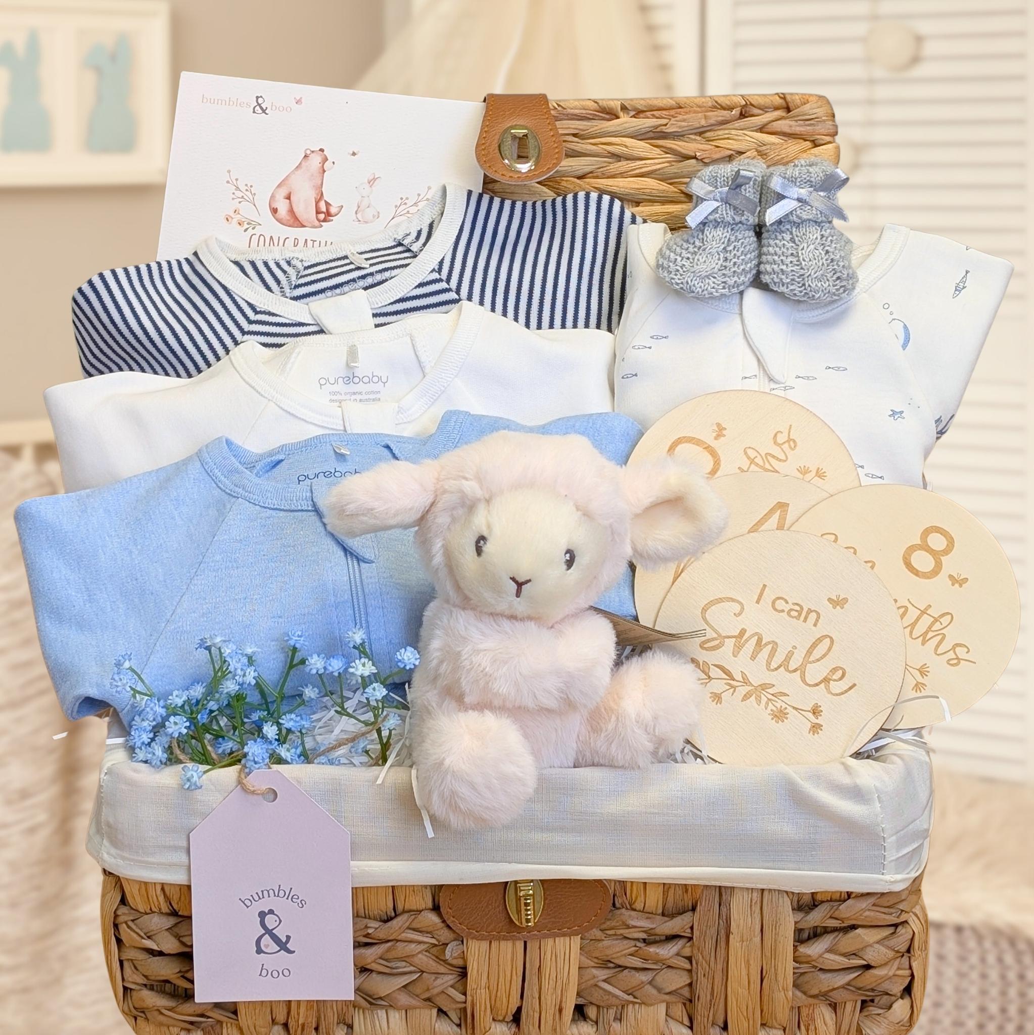Baby boy hamper basket with presents including organic clothing in blue and white with a lamb toy and milestone discs.