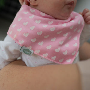 Baby wearing a pink bib with white heart patterns, held by an adult.