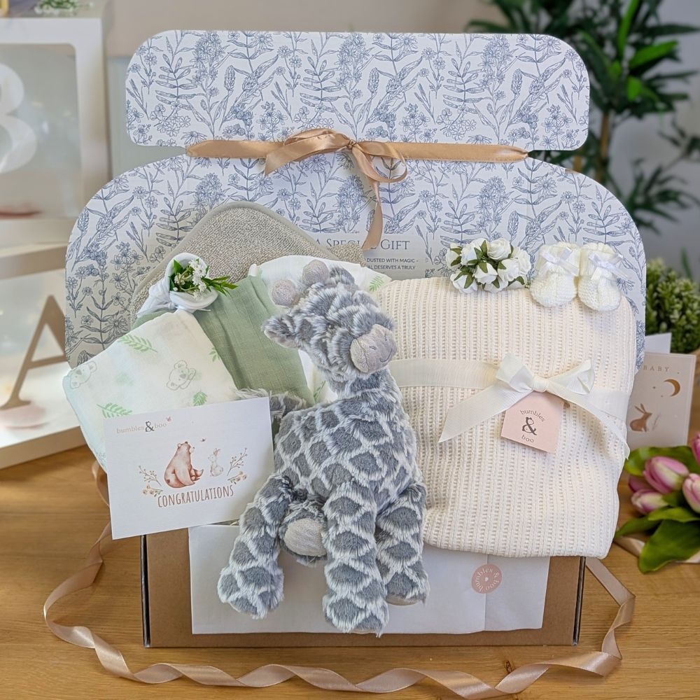 A baby gifts box to welcome a new baby with a grey giraffe soft toy and cream baby blanket.
