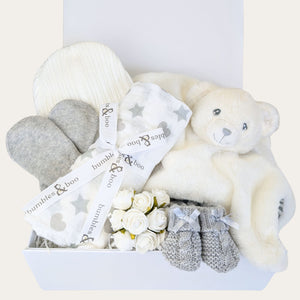 Baby gift set with white teddy bear, gray mittens, and white flowers in a box.
