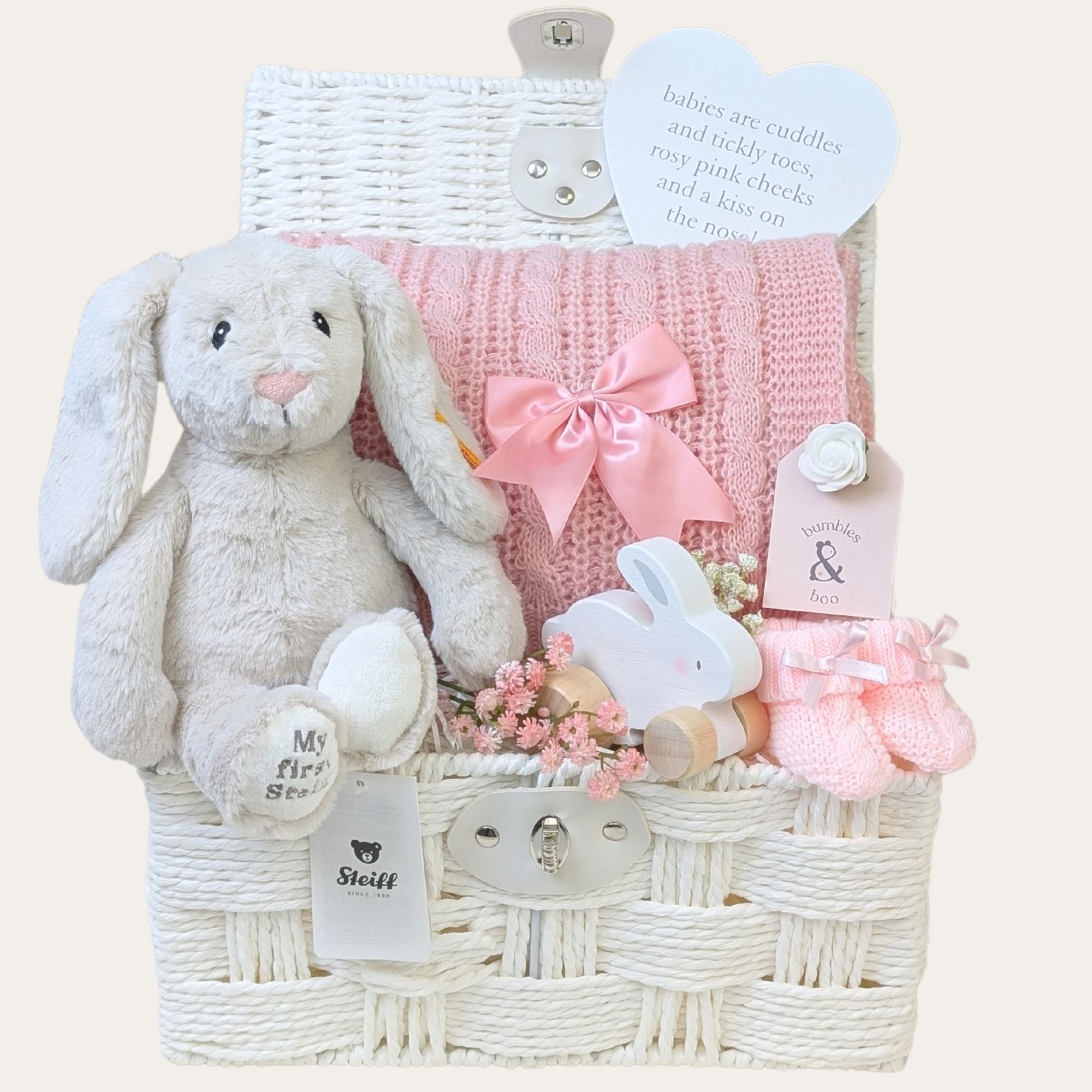 Baby girl gifts packed in a white hamper basket. Gift includes: my first steiff bunny soft cuddly toy, soft pink cable knit blanket and new baby essentials.
