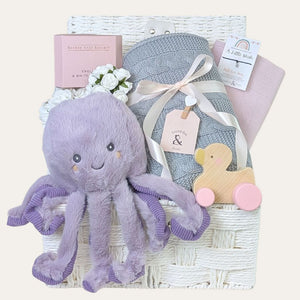 Baby girl gifts hamper basket filled with presents including a purple octopus soft toy.