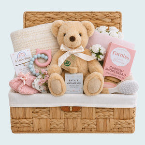 New baby girl gifts in a hamper basket with presents including a teddy bear and biscuits for the new parents.