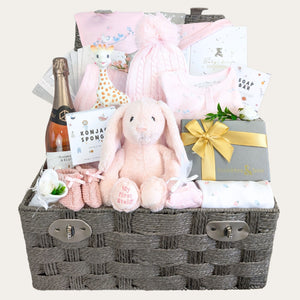 Baby girl gifts in a hamper basket with pink and white presents including pink Steiff bunny and treats for parents.