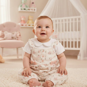 Baby girls long floral dungaree set with bow pockets and white top hanging in nursery wardrobe. Two piece baby clothes outfit.