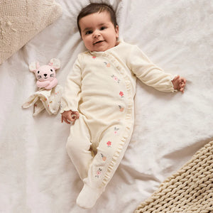 Baby girl wearing cream velour embroidered sleepsuit with matching comforter toy