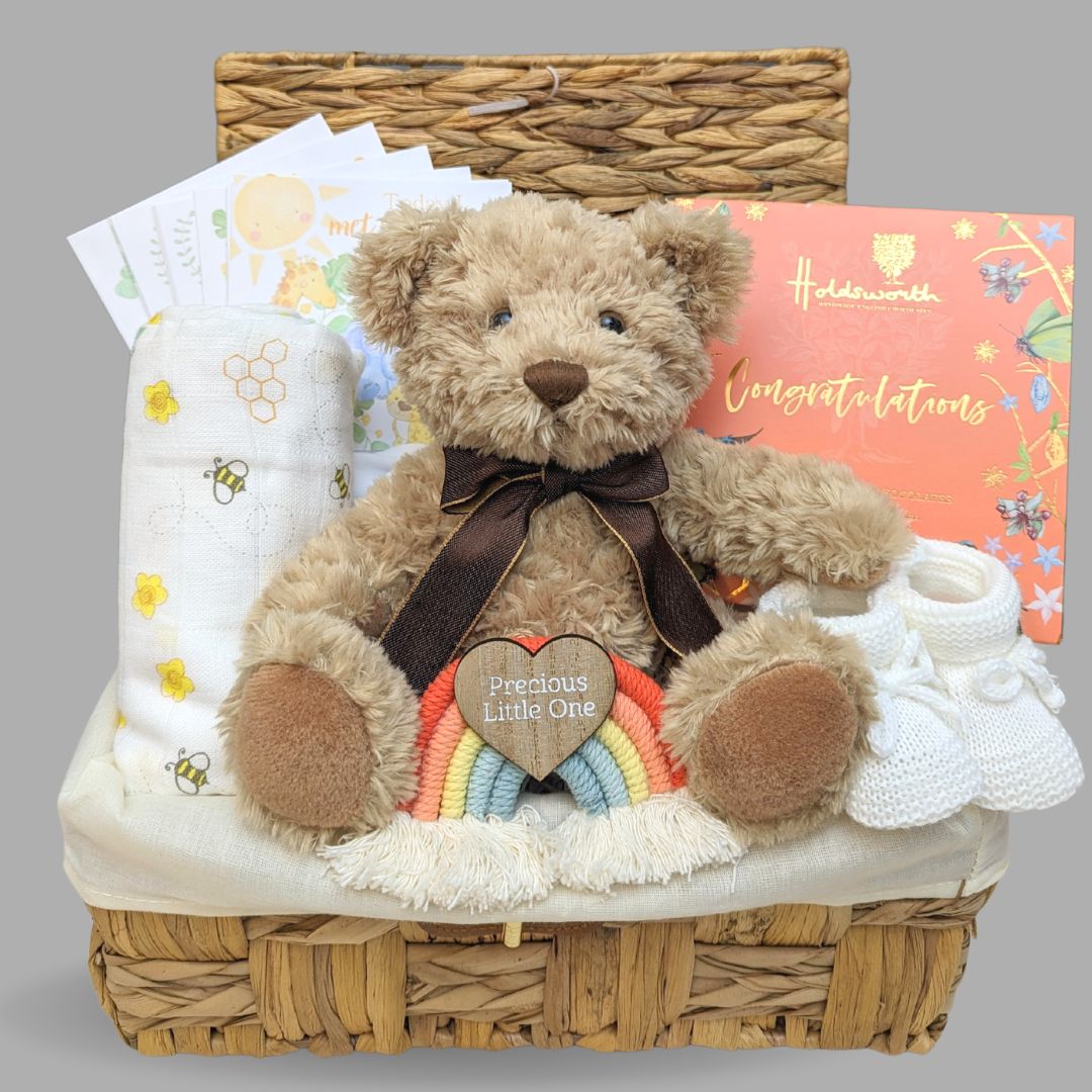 Baby gifts in a hamper basket with teddy bear.