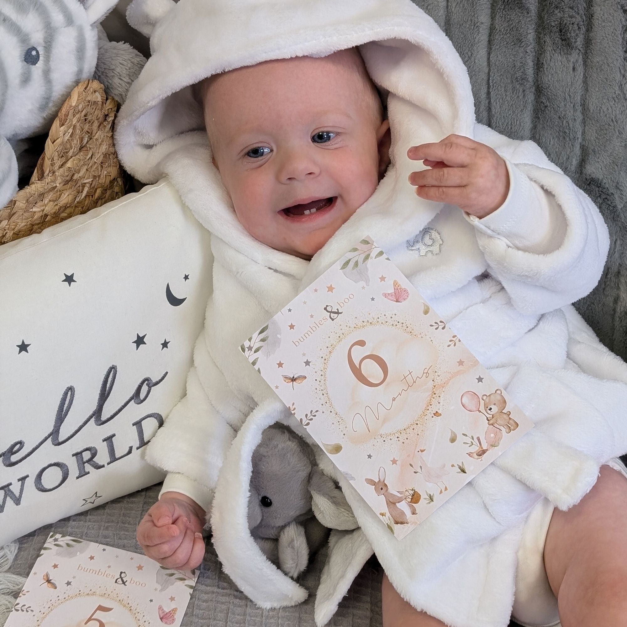 Baby in white dressing gown with a 6 months milestone card. Bumbles and Boo.