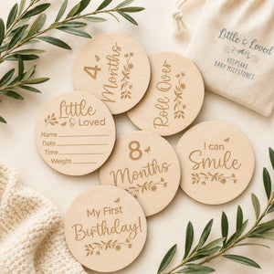 A set of round wooden baby milestone markers with engraved text and floral designs