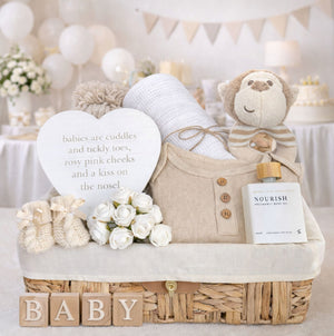 A baby shower bundle of presents to include monkey soft toy and clothing in a hamper basket.