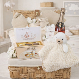 Gift basket with baby items including a baby blanket and teddy bear with chocolates for mum.