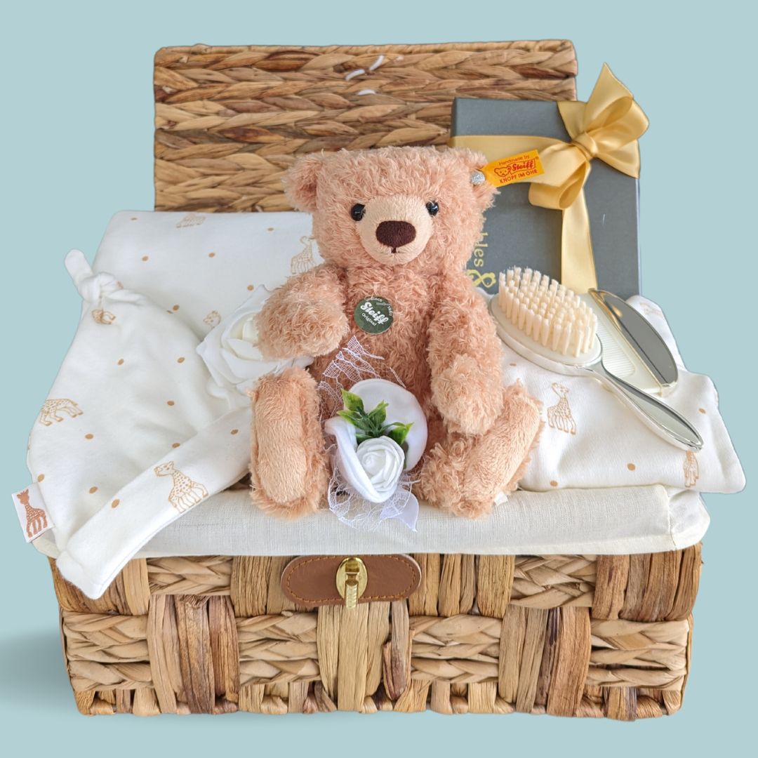 Baby shower gifts hamper with gifts including a traditional teddy bear, silver brush and baby clothes.