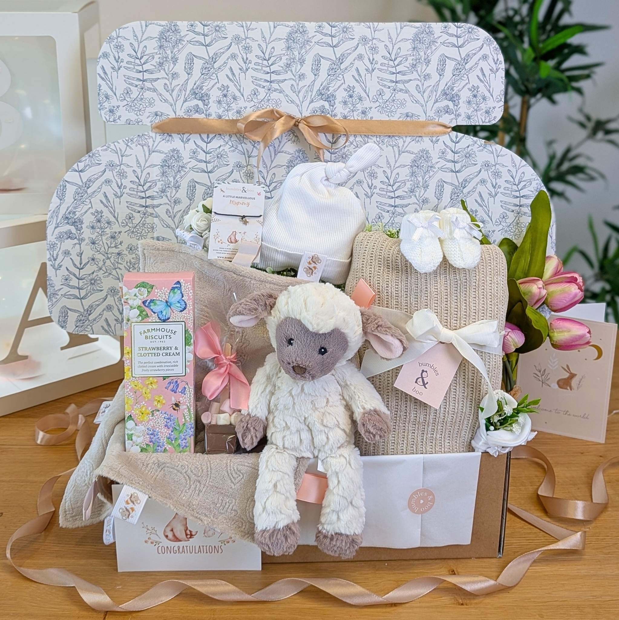 Luxury baby shower gift box beautifully wrapped in tissue and ribbon, filled with neutral baby essentials and treats for mum.