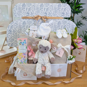 Luxury baby shower gift box beautifully wrapped in tissue and ribbon, filled with neutral baby essentials and gifts for mum.