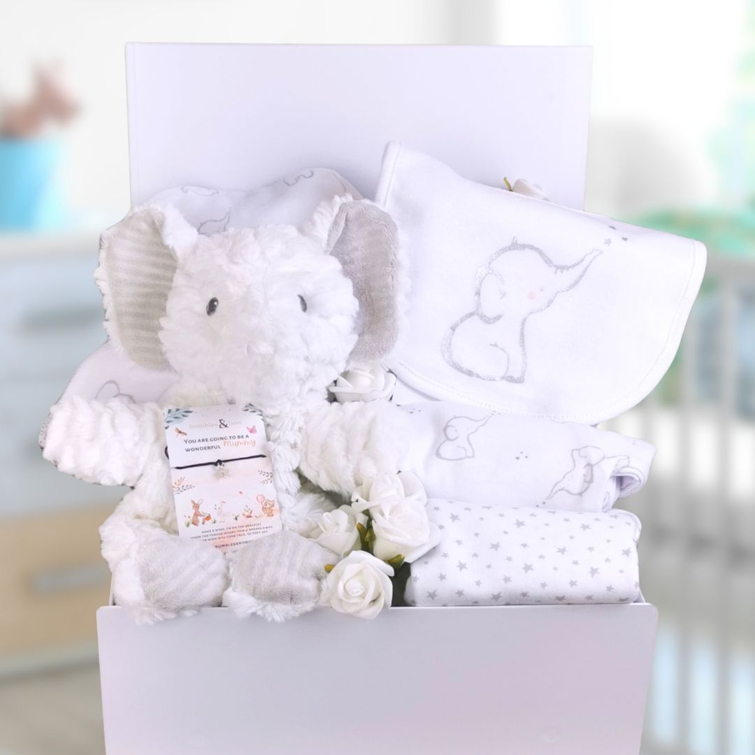 white baby shower gifts in a box with white elephant themed baby clothing and soft toy.