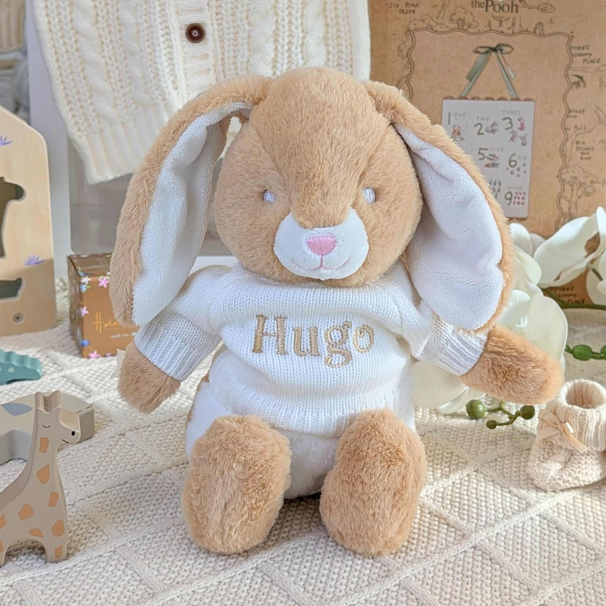 Plush bunny toy with 'Hugo' sweater on a soft surface with toys and decor in the background