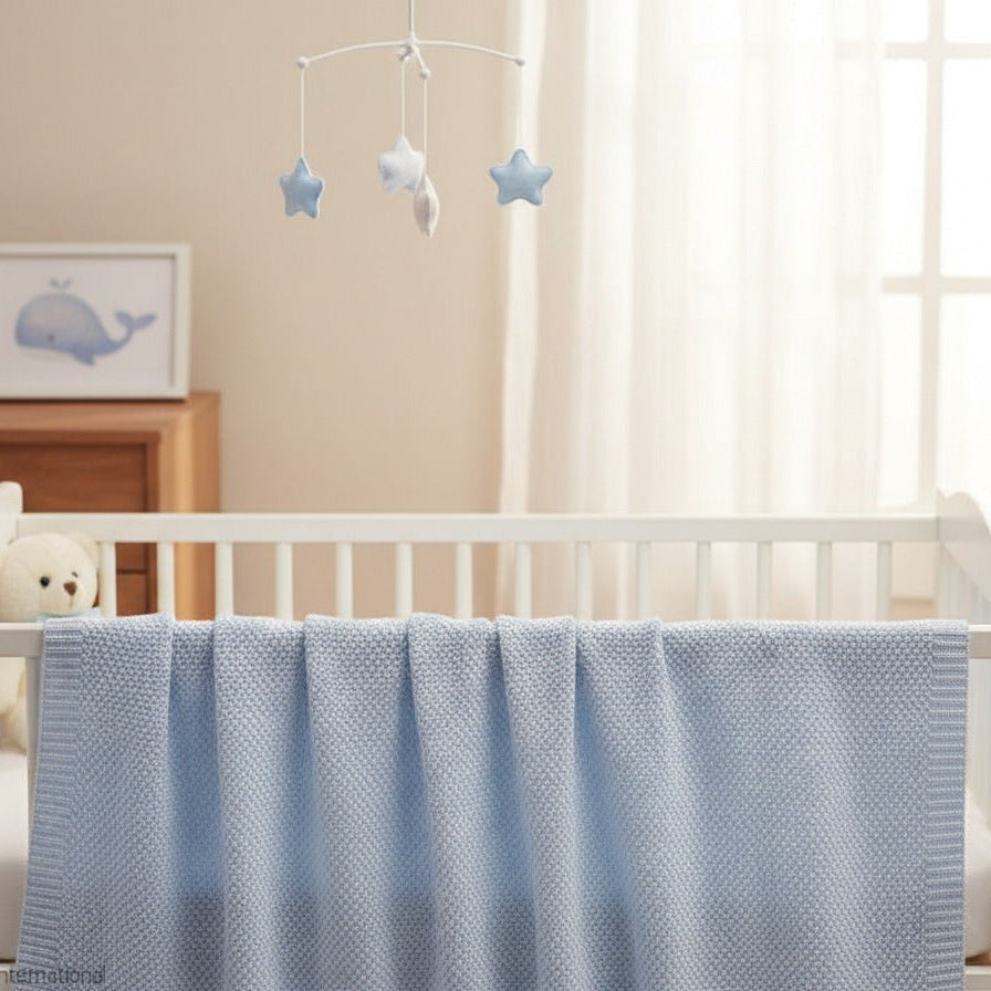 Blue bamboo baby blanket with knitted texture draped over a white cot in a calm nursery