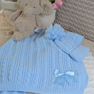 Blue cable knitted baby blanket with a satin bow shown with matching pom pom baby hat.