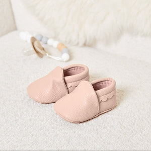Pair of blush pink baby booties with scalloped trim in soft vegan leather, classic baby shoes for newborn baby clothes collection.