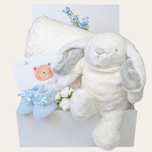 Baby boy gifts hamper with white bunny soft toy and blanket. Presents are packed in a gift box.