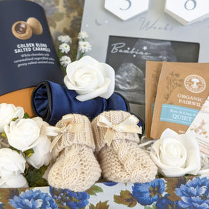 close up of baby knit booties, eye mask for a mum to be and pregnancy countdown frame.