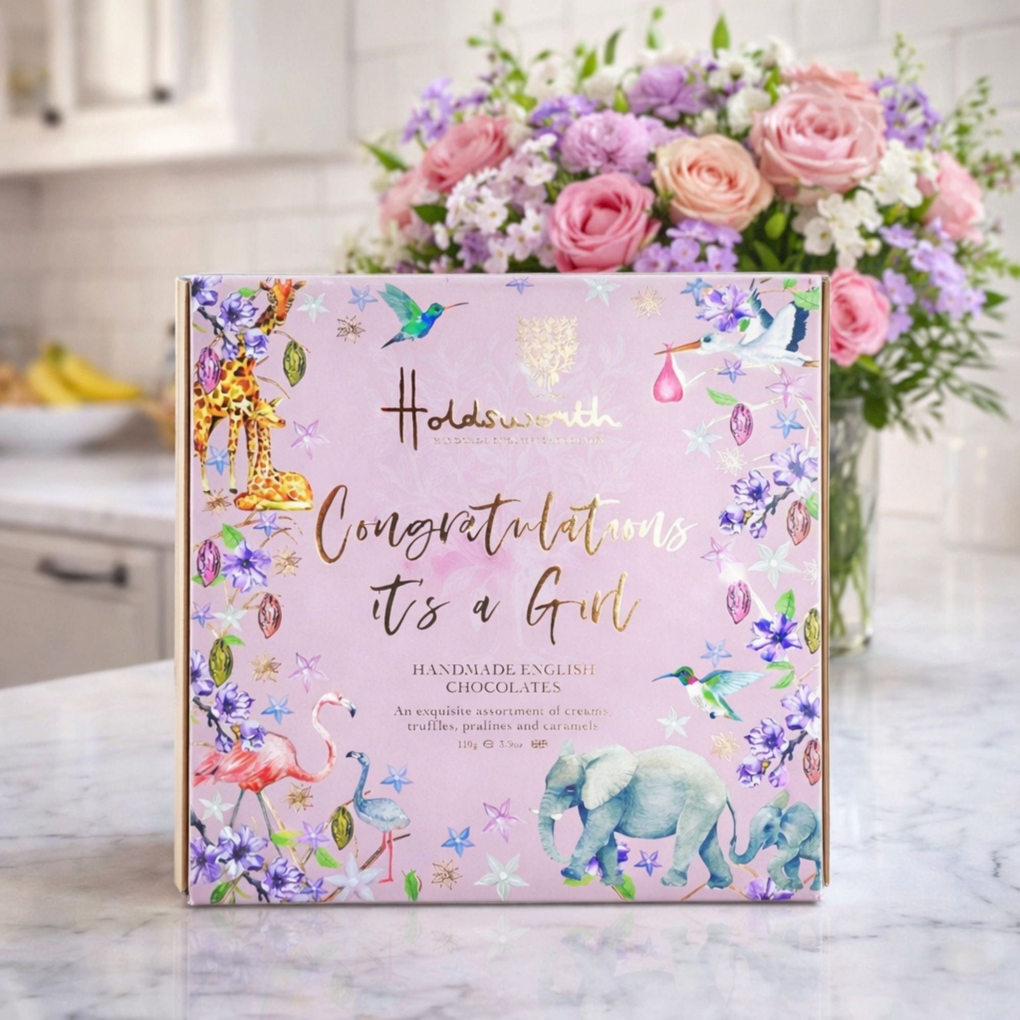 Pink chocolate box with a message on the front for a newborn baby girl ’Congratulations It's A Girl’ On a lifestyle background