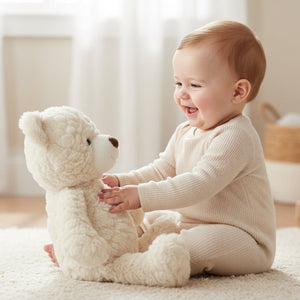 Baby sitting and holding Cream Putty Bear medium teddy, soft neutral plush baby toy with floppy body design.