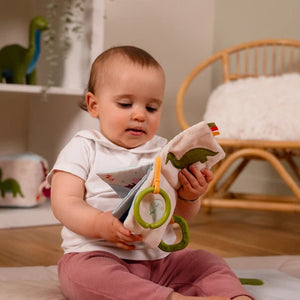Baby holding the Dino Friends Baby Book with teething ring