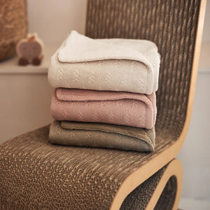 Oatmeal grain knit blanket shown with other colours in same design on chair.