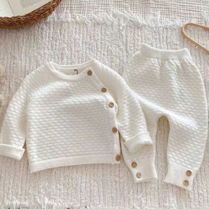 Ivory honeycomb knit baby clothing set with button fastening top and matching trousers placed on soft textured blanket.