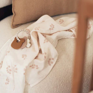 Cream 100% cotton muslin with dusky rose twig print by Jollein. Shown on bed with teether in a lifestyle setting.