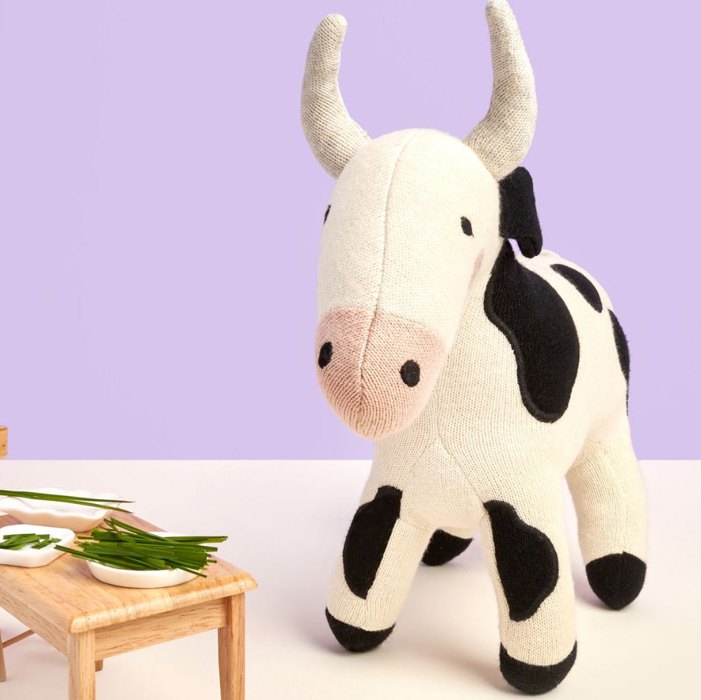 Knitted organic cotton cow soft toy in black and white with stitched face and soft knit texture, suitable for babies