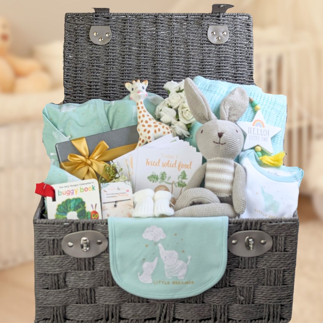 Baby shower gifts in a brown basket with pastel green clothes and blanket, buggy book and bunny toy.