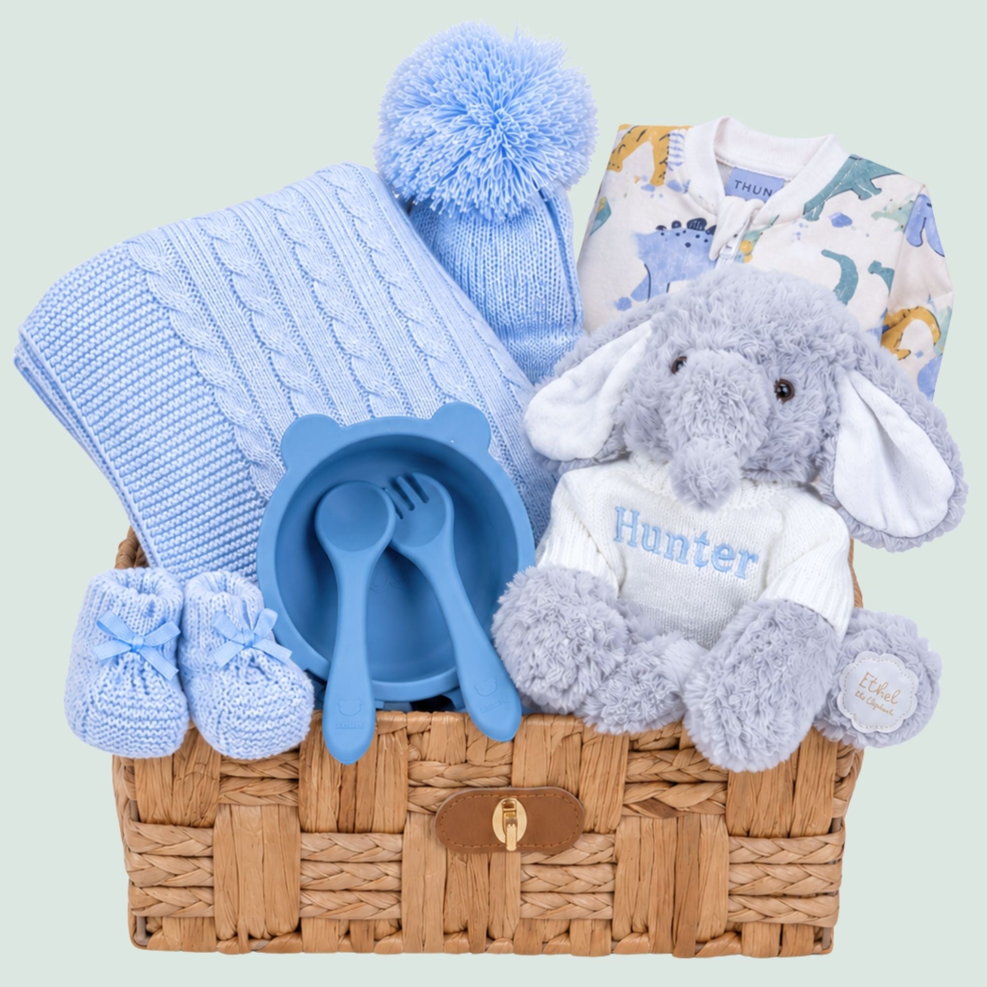Baby boy gifts set with blue knitted blanket and matching hat plus a plush elephant in a hamper basket.