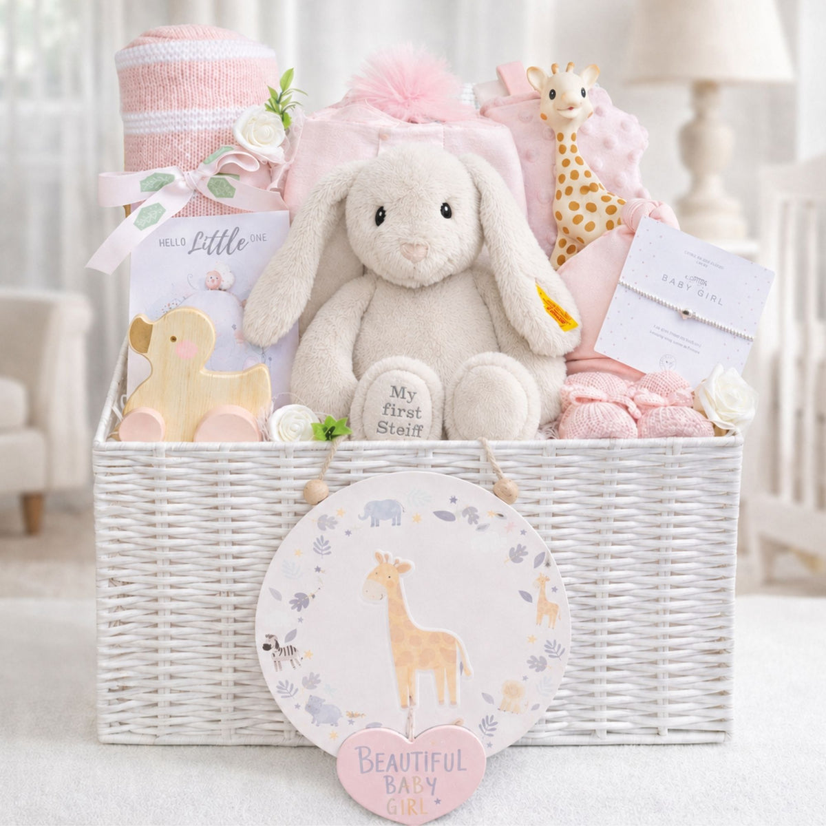 Newborn baby girl hamper basket with gifts including pink steiff bunny, blankets and baby toys in a white basket