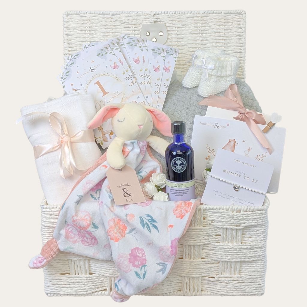 Gifts for mum to be in a white hamper basket. Presents include Neals Yard skincare, milestone cards and a silver mummy to be bracelet. Bumbles and Boo.