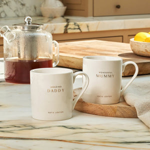 Two mugs labeled 'Mummy' and 'Daddy' on a kitchen counter with a teapot and lemons.