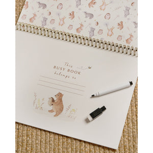 Busy book open to the write-in belongs-to page, with a pen and cap resting on the woven background.