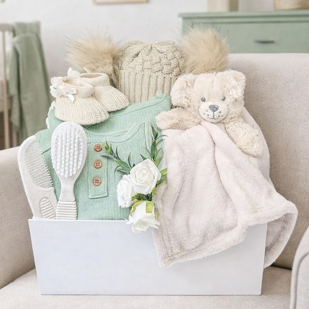 Baby gift box with teddy bear, booties and green clothing to welcome a new baby.