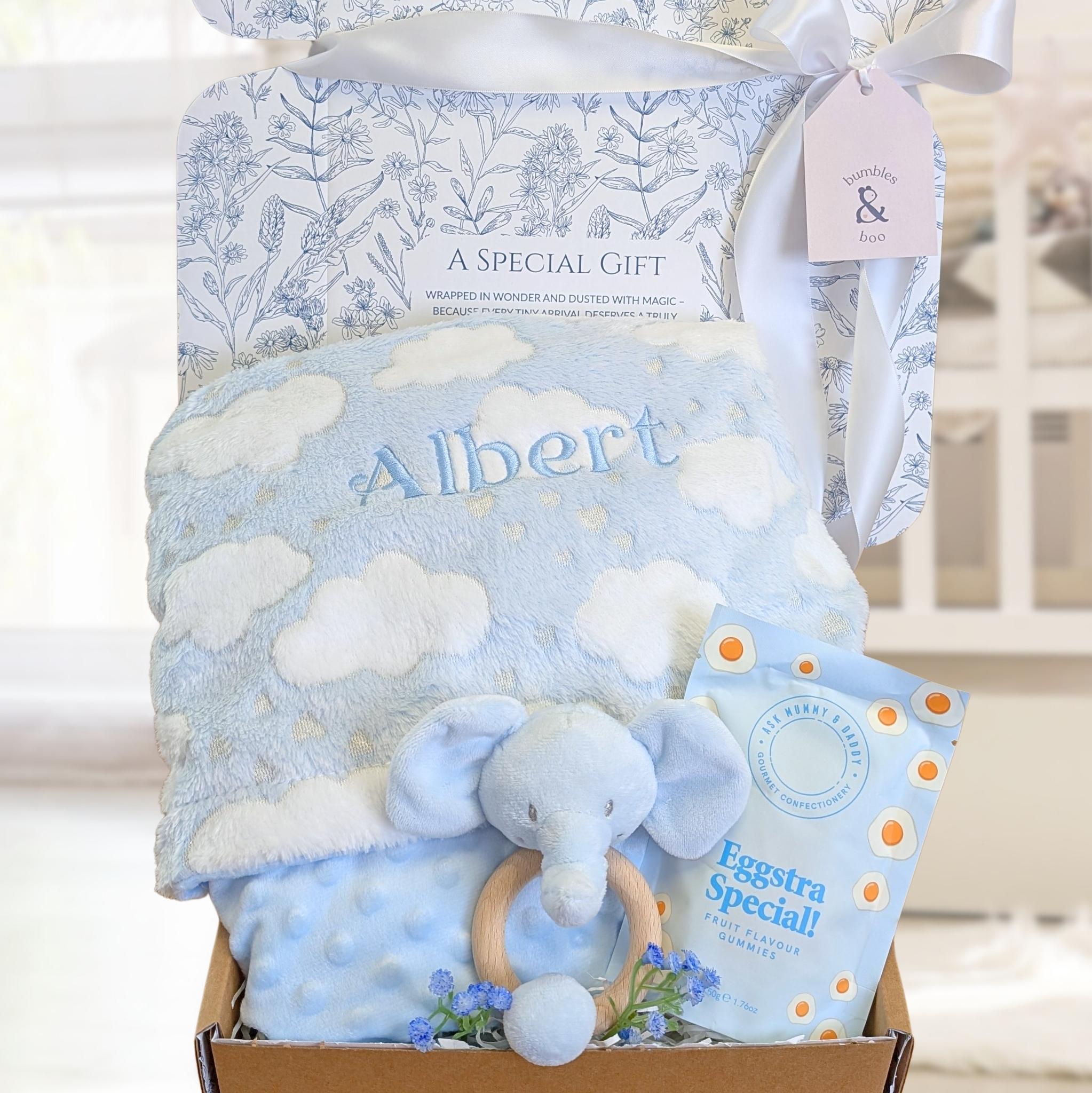 New baby boy gift set with blue elephant toy, blanket, and treat for mum in a box with a white ribbon.