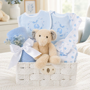 New baby boy gifts in a white hamper basket with blue baby clothes, elephant toy and cellular blanket