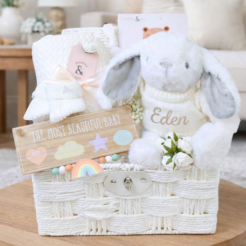 White baby hamper basket full of new baby gifts including bunny and baby blanket.