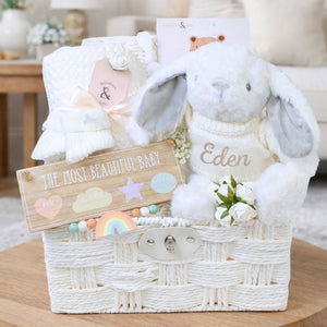 White baby hamper basket full of new baby gifts including bunny and baby blanket.
